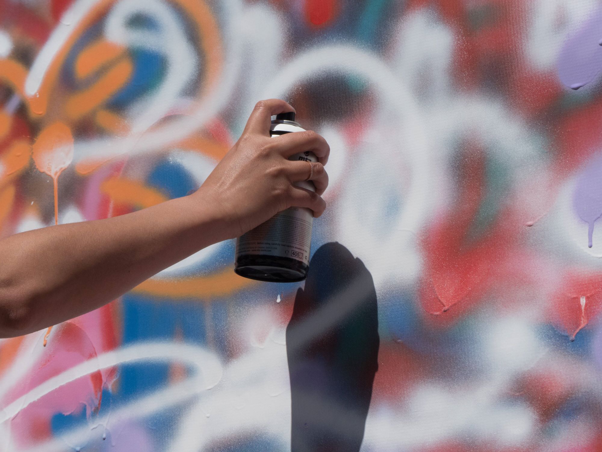 Hand holding a spray paint can painting graffiti on a wall