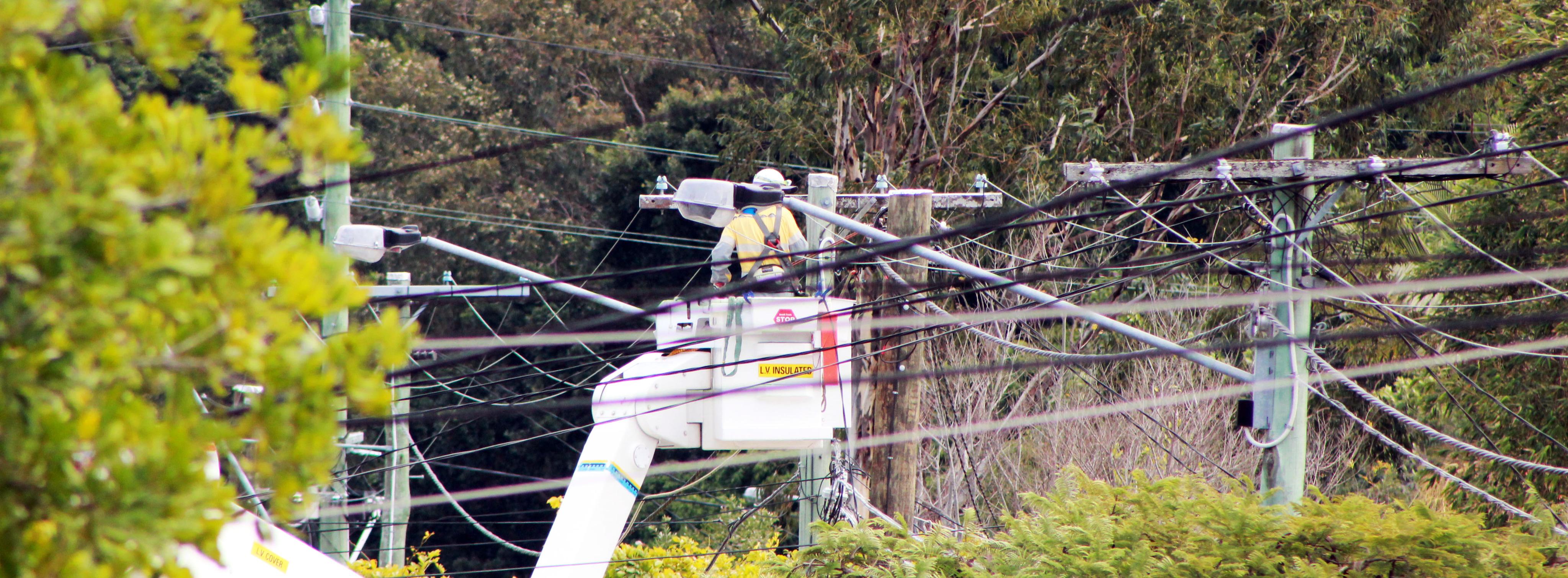 Field crew in cherry picker working near powerlines with trees