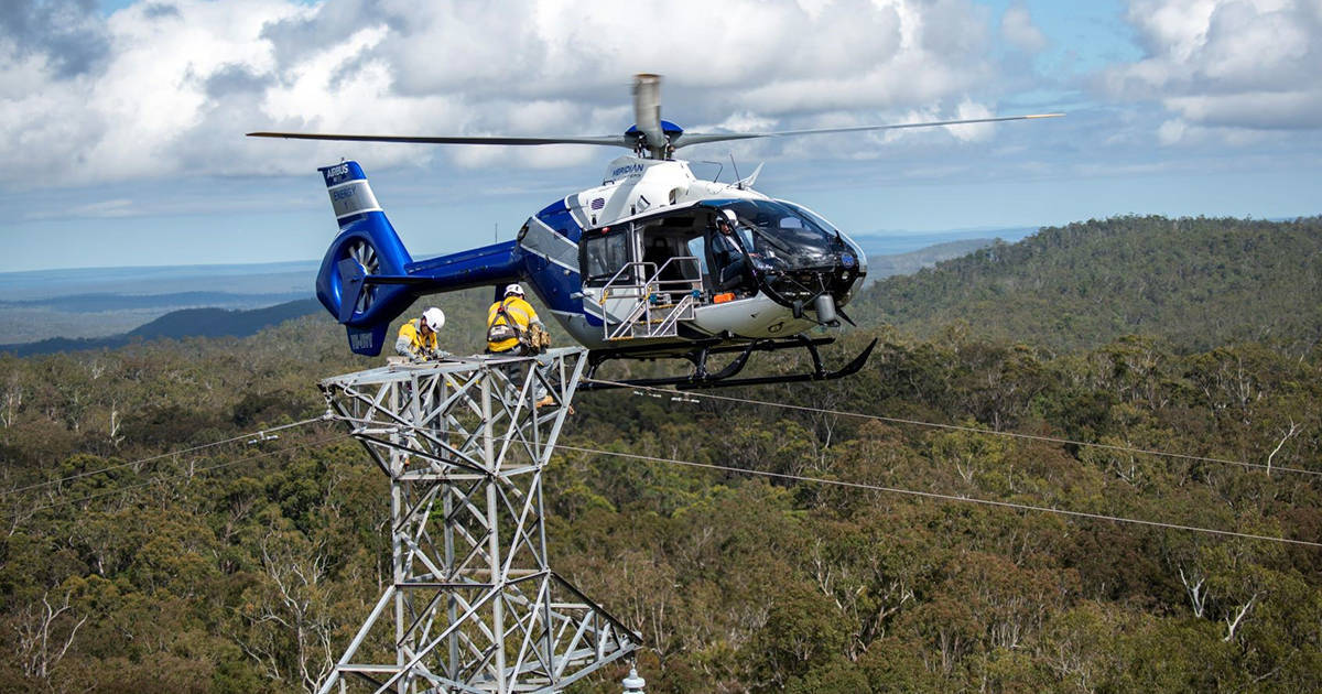 Helicopter assisting crews hang powerline on top of electricity tower