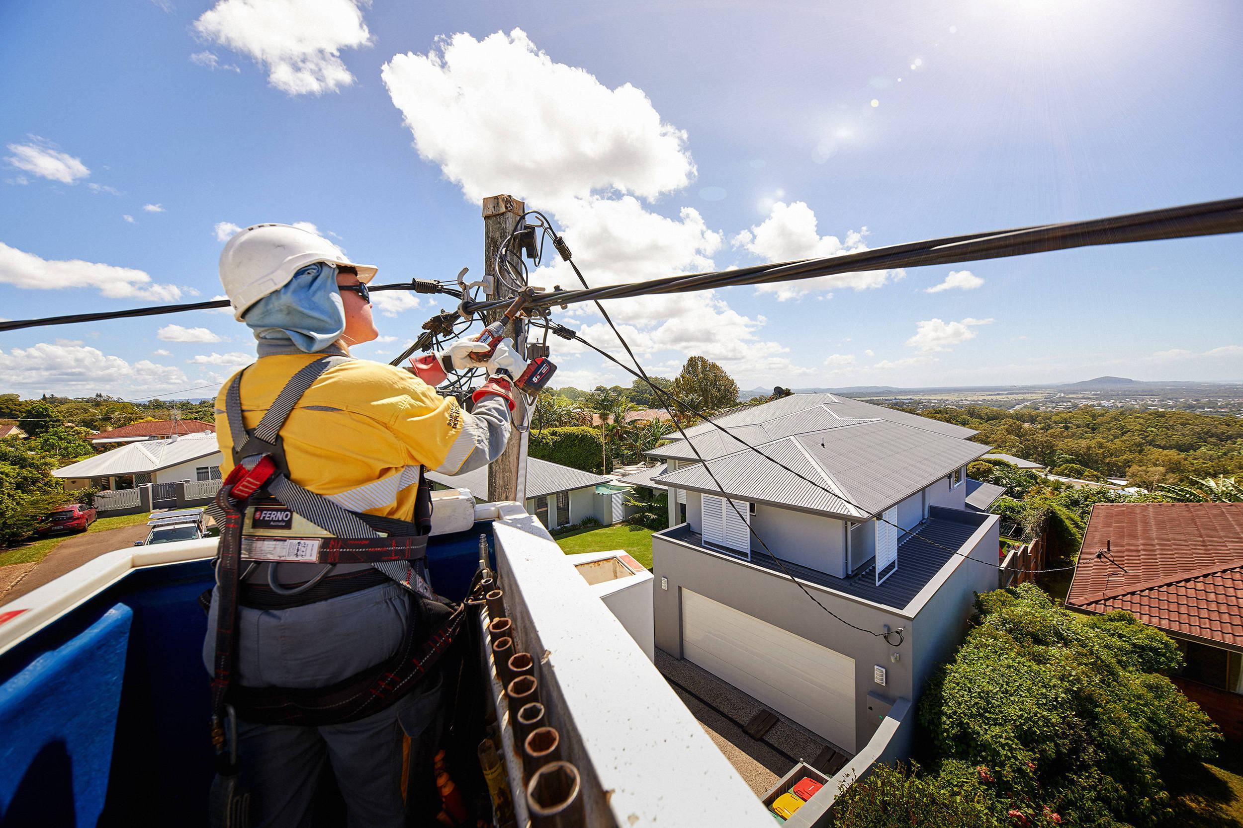 Crew member in a cherry picker working on overhead wires with houses in background