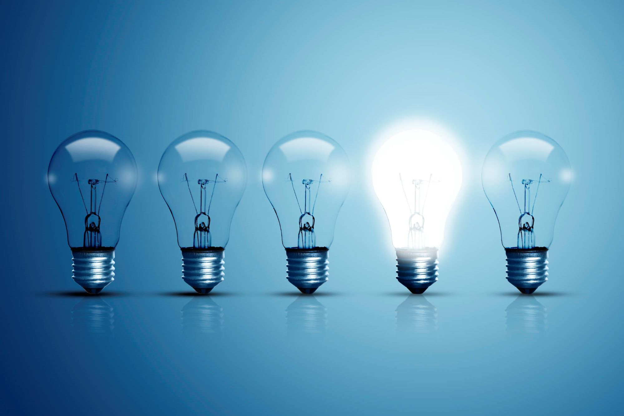 Row of light bulbs on a blue background and one light bulb glowing