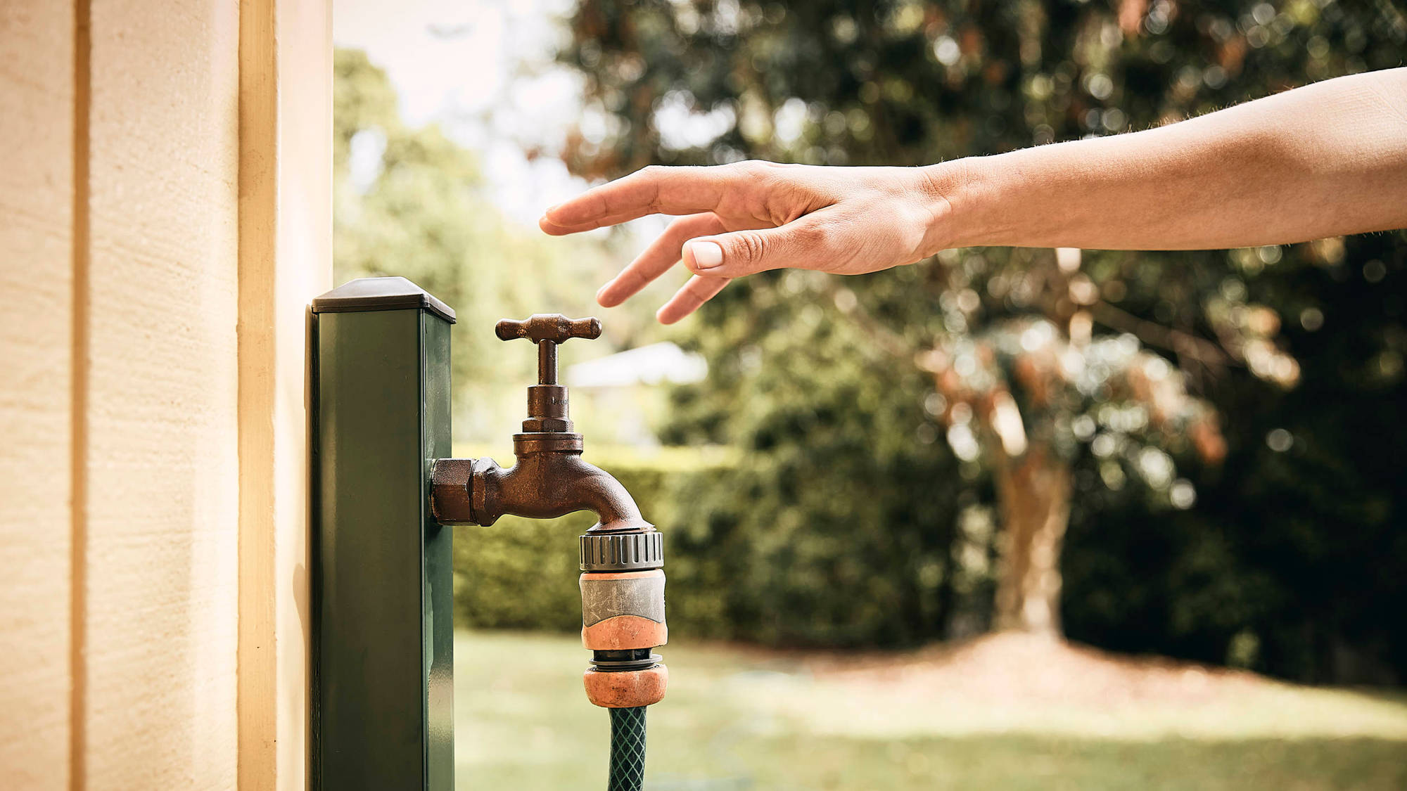 Hand reaching for an outside garden tap.