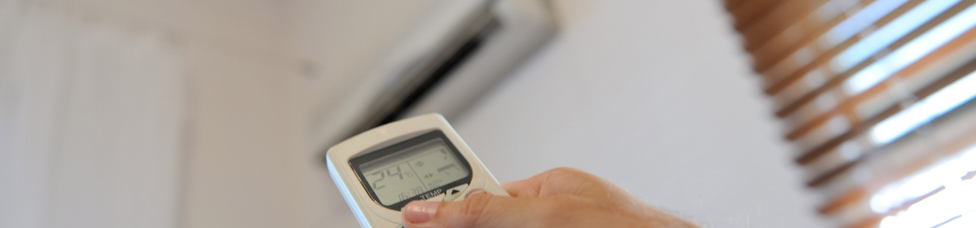 Hand holding remote at air-conditioner