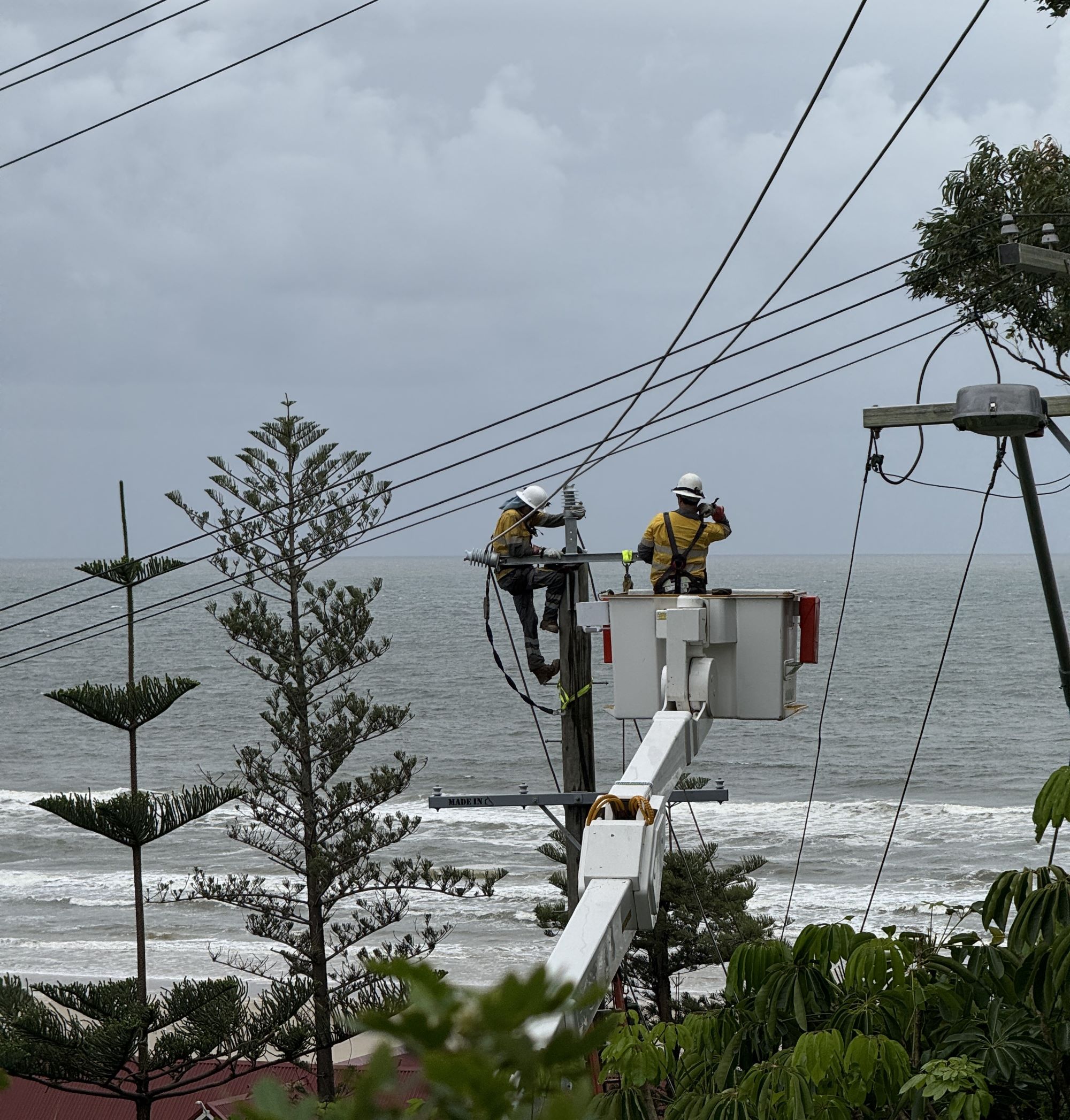 Crews working in a cherry picker on powerlines with ocean in background