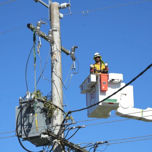 Field crew member gives the thumbs up in cherry picker next to powerlines