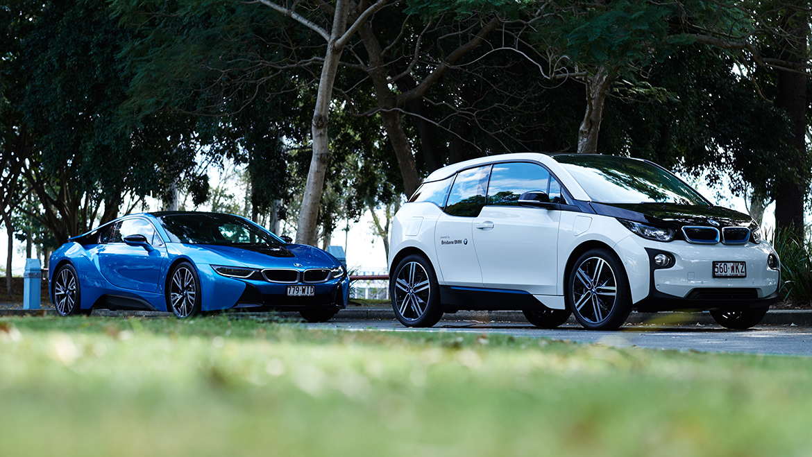 Blue and white BMW electric vehicles lined up on road under trees